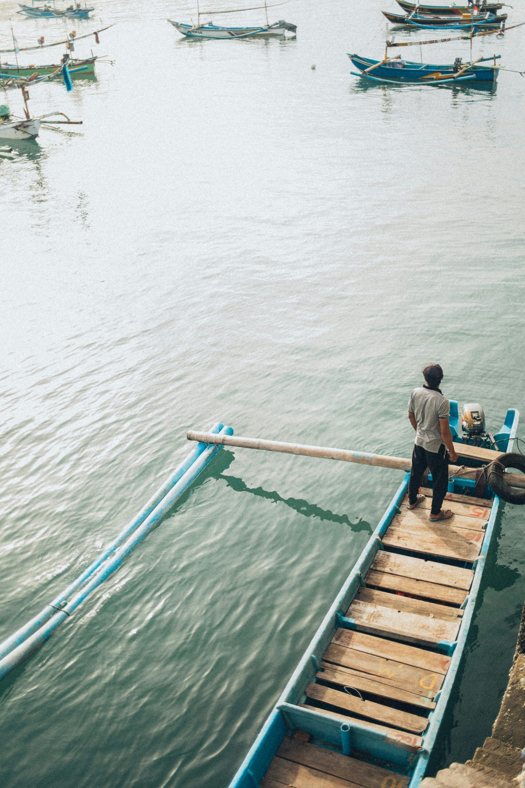 A lone fisherman stands on a traditional wooden boat in calm waters, evoking tranquility.
